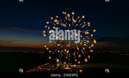 Feux d'artifice dorés explosant dans le ciel nocturne, formant des éclats brillants au-dessus des lumières lointaines de la ville et Une foule rassemblée, avec l'horizon crépusculaire rehaussant l'atmosphère festive. Banque D'Images