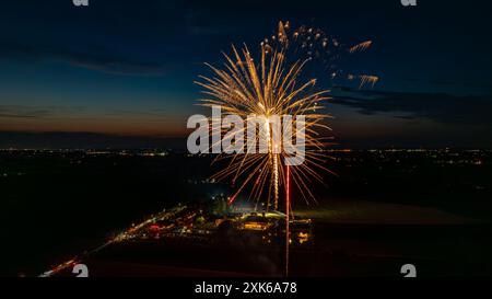 Feux d'artifice dorés explosant dans le ciel nocturne, créant des éclats radieux au-dessus des lumières lointaines de la ville et Une foule rassemblée, avec l'horizon crépusculaire ajoutant à l'atmosphère festive. Banque D'Images