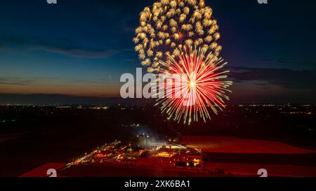 Feux d'artifice rouge vif et doré explosant dans le ciel nocturne, créant des éclats radieux au-dessus des lumières lointaines de la ville et Une foule rassemblée, avec Un horizon crépusculaire ajoutant à l'atmosphère festive. Banque D'Images