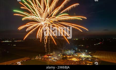 Les feux d'artifice dorés rayonnent brillamment au cours D'Un rassemblement festif, illuminant le ciel nocturne et illuminant le parc d'expositions animé ci-dessous, entouré de vastes champs et de paysages ruraux. Banque D'Images