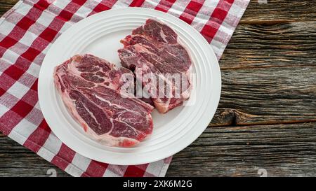 Deux côtelettes d'agneau crues sur une assiette blanche, reposant sur une nappe à carreaux rouge et blanche Banque D'Images