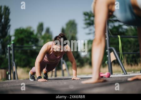 Femmes s'engageant dans l'entraînement de fitness en plein air dans le parc ensoleillé, effectuant des exercices de calisthenics Banque D'Images