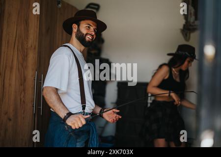 Heureux jeune couple portant des chapeaux préparant l'équipement d'équitation dans une salle de stockage rustique Banque D'Images