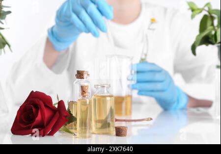 Produit d'aromathérapie. Scientifique développant des huiles essentielles à table blanche en laboratoire, focus sur les bouteilles et la rose Banque D'Images