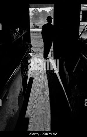 Macédoine, Arkansas, États-Unis – 27 juin 2024 : photo horizontale du propriétaire du magasin penché dans la porte d’entrée du magasin en silhouette devant lui Banque D'Images