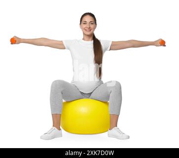 Belle femme enceinte avec des haltères faisant des exercices sur fitball sur fond blanc Banque D'Images