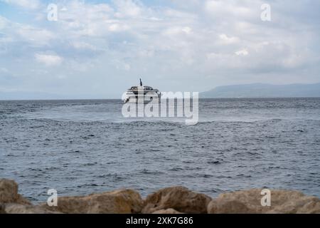 Seascape. Un grand paquebot touristique flotte sur les vagues jusqu'à l'île. Montagnes à l'horizon. Au premier plan se trouvent de grosses pierres. navire en mer Banque D'Images