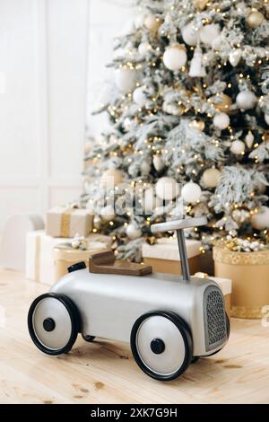 Voiture d'enfants vintage sur un fond flou d'un arbre de Noël avec des cadeaux, des jouets et du bokeh des lumières des guirlandes. Faible profondeur de champ Banque D'Images