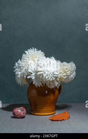 Nature morte avec des fleurs, feuilles jaunes sur un fond sombre. Dahlias blancs dans un vase, feuilles jaunes, coeur rose. Placer pour le texte Banque D'Images