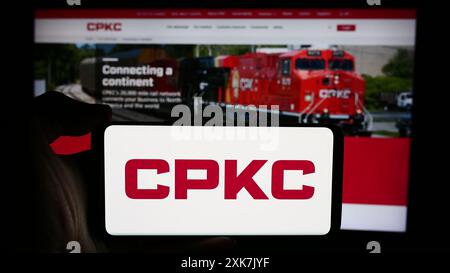 Personne tenant un téléphone cellulaire avec le logo de la compagnie de chemin de fer canadien Pacifique Kansas City Limited (CPKC) devant la page Web. Concentrez-vous sur l'affichage du téléphone. Banque D'Images