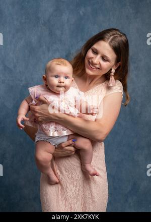 Une jeune mère aux cheveux longs dans une robe légère tient une fille nouveau-née dans ses bras. L'amour de maman Banque D'Images