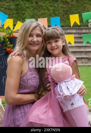 Maman embrasse fermement sa petite fille, qui est allée en 1re année. La fille tient une corne d'école. Sur le fond d'un conseil scolaire et multicolore Banque D'Images