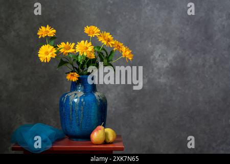 Tranquillité et confort sur une table rouge en bois. Deux poires jaunes, un bouquet de fleurs jaunes d'automne dans un grand vase en argile bleue. Fond gris foncé. Banque D'Images