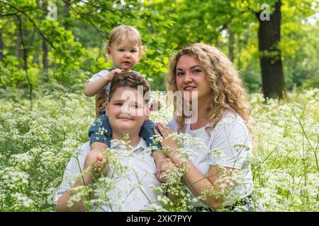 Maman avec deux fils dans l'herbe épaisse. Le frère aîné tient un petit bébé, âgé d'un an, sur ses épaules. Heureuse famille Banque D'Images