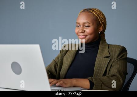 Confiant jeune femme d'affaires noire dans le tapage de vêtements d'affaires sur ordinateur portable dans le bureau Banque D'Images