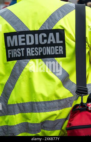 Le dos d'un premier intervenant médical portant un manteau uniforme jaune vif avec une croix réfléchissante grise. Le Service médical d'urgence transporte un sac Banque D'Images