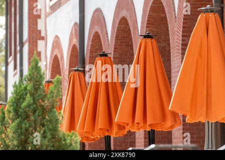 Plusieurs grands parasols d'été en nylon ombragé, de couleur orange, fermés avec des supports en bois brun. Les capots de protection solaire ne sont pas ouverts. Banque D'Images