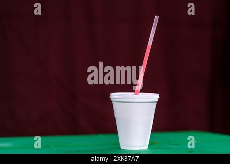 Un grand gobelet blanc à emporter non recyclable avec un couvercle en plastique et de la paille sur une table de patio vert vif. Le polystyrène est une tasse isolée en polystyrène Banque D'Images