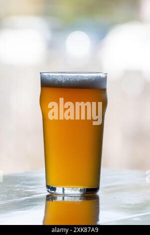 Un verre à pinte transparent contient une bière artisanale lager. La bière, bière brassée est sur le coin d'une table en bois. Le dessus du rafraîchissement d'alcool est blanc Banque D'Images