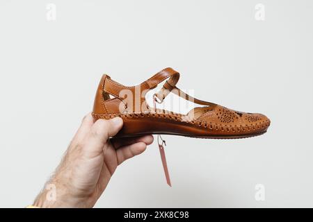 Une main masculine tient une paire de chaussures d'été tricotées féminines sur un fond blanc, soulignant le design et la texture de la chaussure Banque D'Images