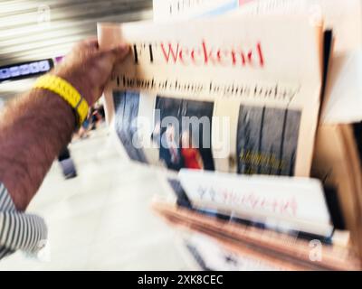 Palma, Espagne - 11 juillet 2024 : une vue défocalisée montre une main masculine qui tend vers le journal FT Weekend depuis un stand dans un quartier animé, capturant l'agitation de la vie urbaine. Banque D'Images