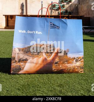 Palma, Espagne - 11 juillet 2024 : un sac en papier pour chaussures Camper, avec le texte Walk, Donât Run et un drapeau grec, est laissé dans un jardin à Majorque, en Espagne, mettant en valeur un cadre extérieur dynamique et élégant Banque D'Images