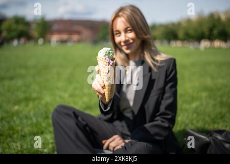 Délicieuse crème glacée verte dans un cône de gaufre tenu par une femme au foyer flou dans le parc vert dans la chaleur estivale Banque D'Images