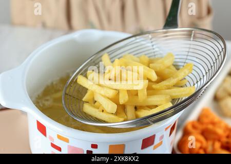 Gros plan cuisson des frites à la maison, friture profonde des bâtonnets de pommes de terre surgelés dans de l'huile chaude. Frites sur treillis métallique Banque D'Images