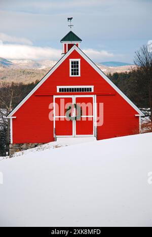Une grange rouge entourée de neige hivernale est décorée d'une couronne de Noël dans les hautes terres de la Nouvelle-Angleterre Banque D'Images