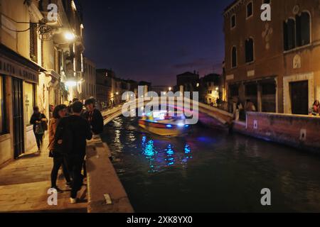 Les amis apprécient les boissons du soir et cicchetti au bord du canal sur Dorsoduro à Venise, en Italie, tandis qu'une ambulance aquatique passe sous un pont près de Rio S. Trovaso Banque D'Images