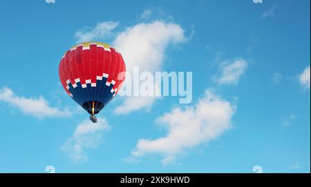Montgolfière en bleu foncé, rouge et jaune volant dans un ciel bleu légèrement nuageux Banque D'Images