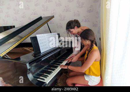 Femme hispanique dans ses 30 ans donnant des leçons de piano à une adolescente à la maison avec un piano à queue. Le professeur corrige la position du h de l'élève Banque D'Images