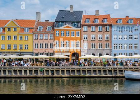 Copenhague Danemark 21 juillet 2024, Une scène de rue animée à Copenhague avec des bâtiments colorés bordant un canal, avec une salle à manger extérieure animée où les clients apprécient un repas par une journée ensoleillée. Banque D'Images