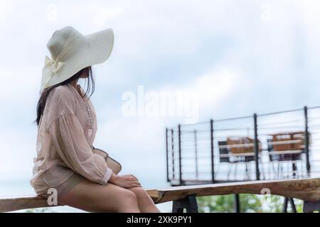 Une femme élancée dans une robe blanche est assise seule dans un café sur un point de vue élevé et profite d'un coucher de soleil coloré sur la vallée. en arrière-plan mer et Banque D'Images