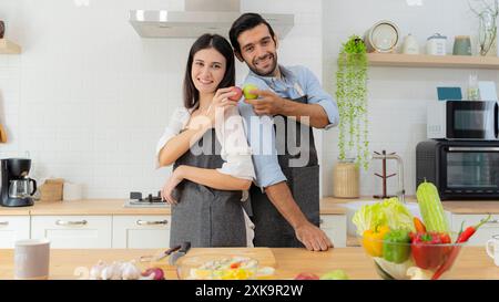 Couple attrayant tenant des pommes rouges et des pommes vertes dans leurs mains. Un jeune couple amoureux s'amusant tout en préparant un petit déjeuner ensemble sur un beau Banque D'Images