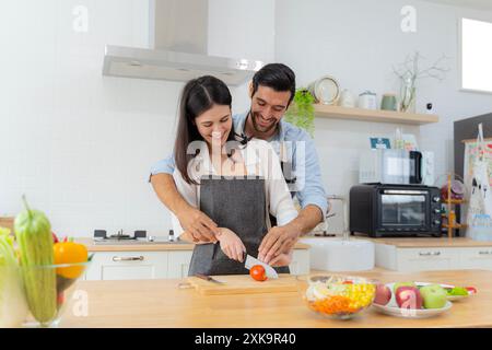 Jeune couple s'amusant tout en préparant le petit déjeuner ensemble dans une belle matinée, cuisiner ensemble, relation cuisine, trancher les tomates ensemble. L Banque D'Images
