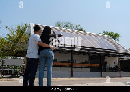 La famille utilise un système d'énergie renouvelable avec panneau solaire. Vue arrière d'Un jeune couple debout devant leur nouvelle maison, un module solaire par une journée ensoleillée, Banque D'Images