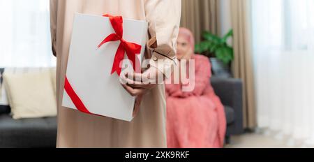 Mari musulman donnant une boîte-cadeau emballée à la femme surprise célébrant les vacances de Noël ou la Saint-Valentin ensemble assis sur le canapé à la maison. Vacances ce Banque D'Images