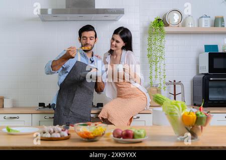 L'homme qui inhalait l'odeur du petit déjeuner en cours de préparation avec sa petite amie à proximité. Couple amoureux s'amuser tout en préparant un petit déjeuner ensemble Banque D'Images