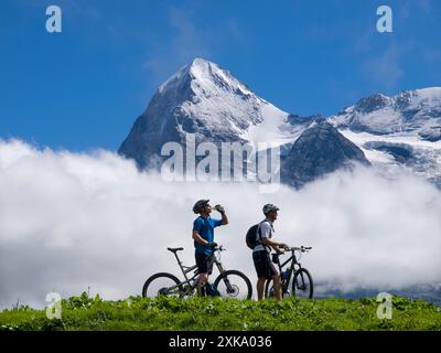 Deux vététistes se reposent et boivent près du village de Murren, lors d’une longue balade à vélo dans l’Oberland bernois. En arrière-plan la célèbre montagne Eiger. Banque D'Images