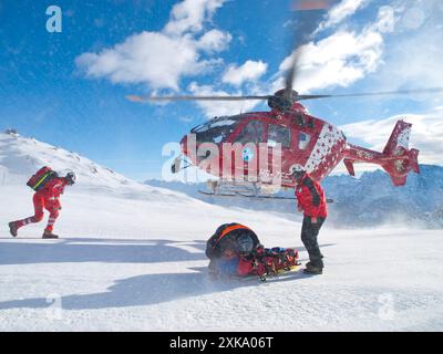 Un hélicoptère de sauvetage atterrit à côté d'un skieur blessé. Le paramédical et le médecin ont traité le patient sur la piste de ski après qu'il a percuté un snowboarder. Air Zermatt en Suisse Banque D'Images