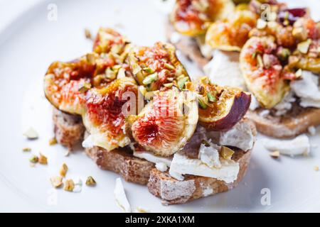 Pain grillé au fromage feta, figues et pistaches sur une assiette blanche, fond blanc. Banque D'Images