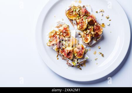 Pain grillé petit déjeuner avec fromage feta, figues et pistaches sur une assiette blanche, fond blanc, vue de dessus. Banque D'Images