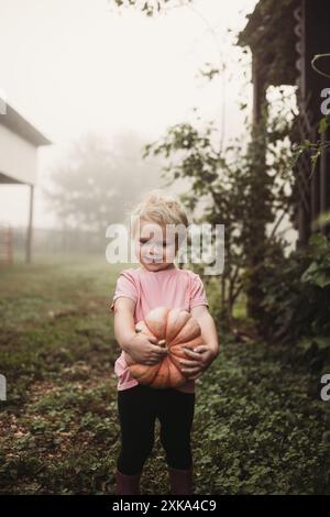 Enfant tenant la citrouille dans la cour le jour brumeux Banque D'Images