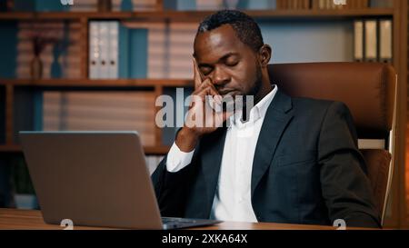Fatigué homme d'affaires triste assis dans le bureau somnolent épuisé homme afro-américain gestionnaire professionnel travailleur s'endort sur le lieu de travail sieste penchant Banque D'Images