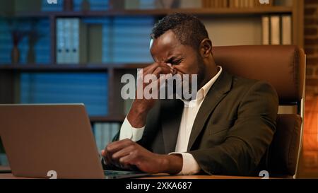 Homme d'affaires afro-américain adulte travaillant sur ordinateur portable dans le bureau homme fatigué malsain souffrant de maux de tête ressent la fatigue de pression de douleur du surmenage Banque D'Images