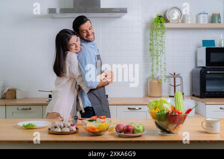 Une femme embrasse joyeusement un homme, un couple heureux. Jeune couple amoureux s'amuser tout en préparant un petit déjeuner ensemble par une belle matinée. Cuisine, toge Banque D'Images