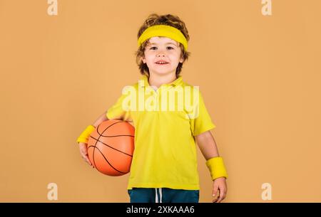 Petit basket-ball en vêtements de sport avec ballon de basket-ball. Garçon enfant souriant en t-shirt jaune avec basket-ball. Sport, mode de vie actif, santé, équipe Banque D'Images