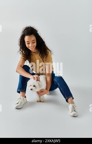 Une jeune femme caresse paisiblement sa frise de bichon moelleuse à la maison. Banque D'Images