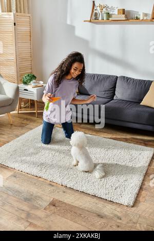 Jeune femme jouant joyeusement avec son chien Bichon Frise sur un tapis confortable. Banque D'Images